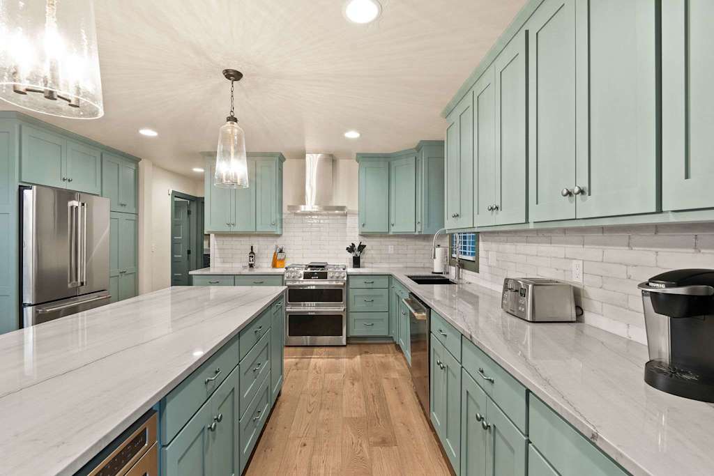 The Tamarack — modern kitchen with teal cabinets, marble countertops, stainless steel appliances, and large island
