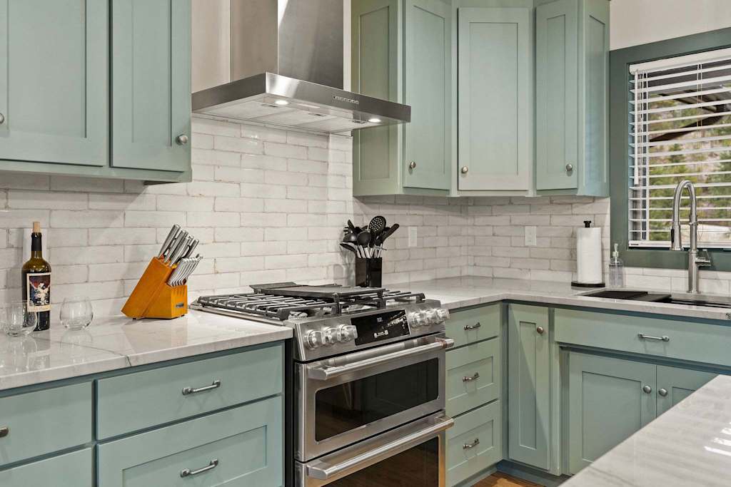 The Tamarack — stainless steel range and hood with white subway tile backsplash and light green cabinets