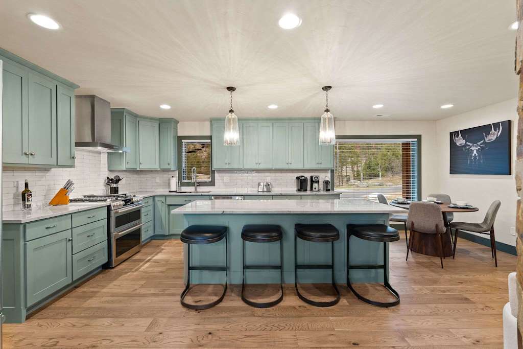 The Tamarack — kitchen with light teal cabinets, a large island with four barstools, and stainless steel appliances