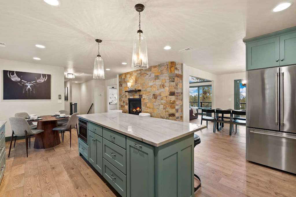 The Tamarack — kitchen island facing a stone accent fireplace wall, stainless steel refrigerator, and dining area