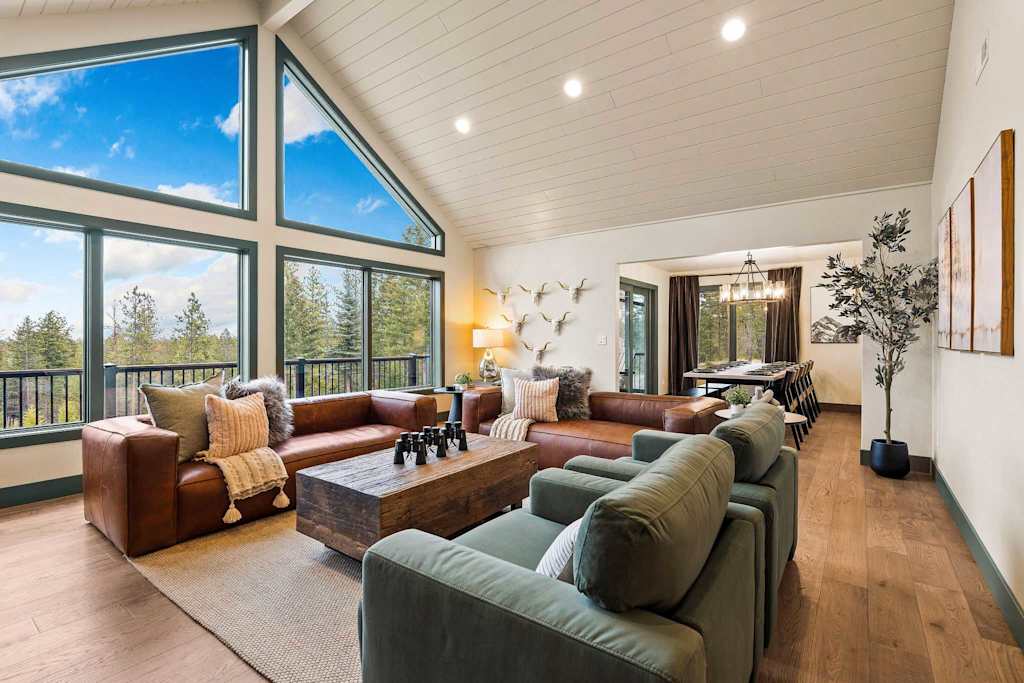 The Tamarack — living room with vaulted ceilings, large windows, brown leather couches, and green armchairs