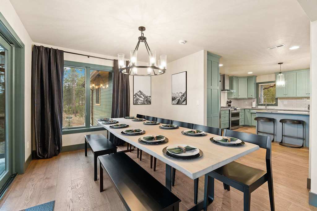 The Tamarack — long dining table with bench and chairs under a chandelier, adjacent to the kitchen