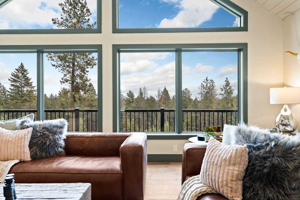 The Tamarack — brown leather seating with pillows situated in front of large windows overlooking evergreen trees