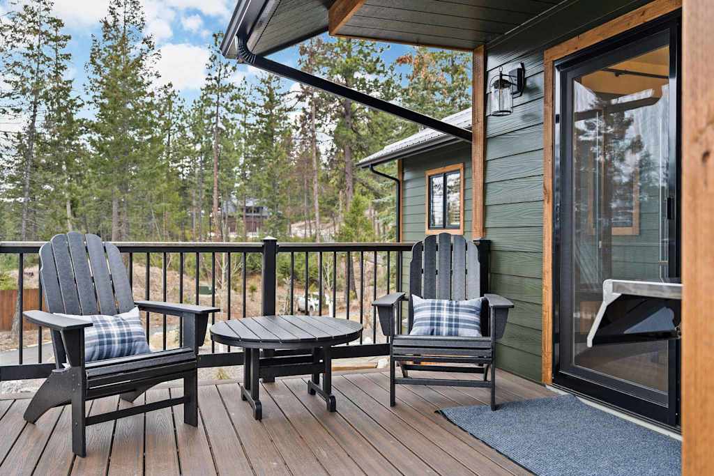 The Tamarack — outdoor deck with two adirondack chairs, a round table, and a view of pine trees