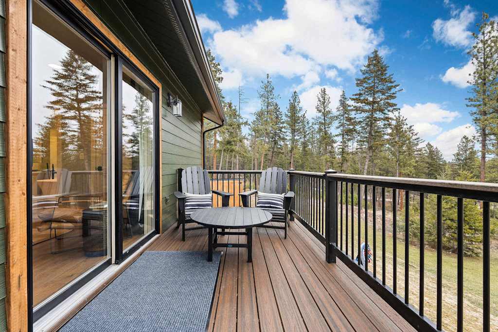 The Tamarack — wooden deck with chairs, small table, sliding glass door, and forest view beyond railings