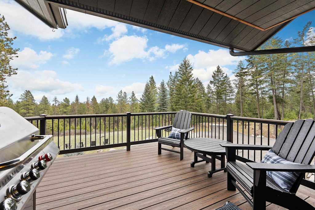 The Tamarack — outdoor deck featuring a stainless steel grill, chairs, table, and pine tree views