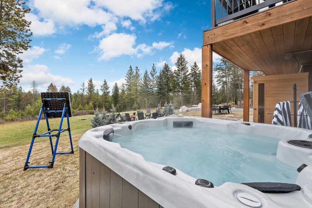 The Tamarack — steaming outdoor hot tub on patio overlooking lawn, trees, and a target stand