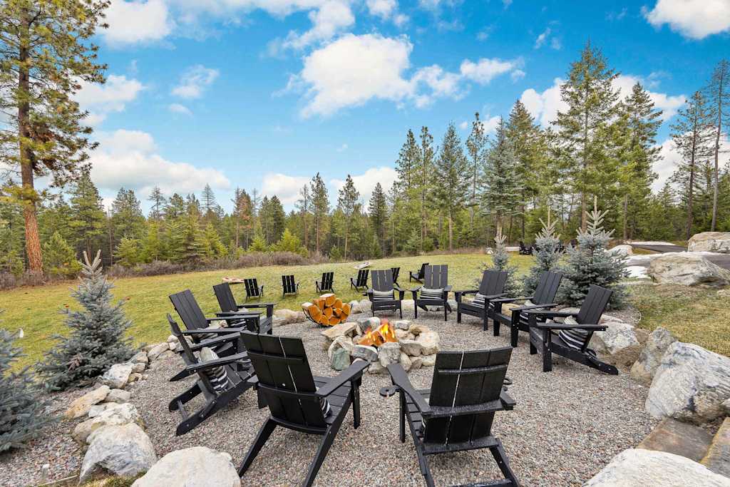 The Tamarack — stone fire pit with active fire encircled by black adirondack chairs in gravel yard