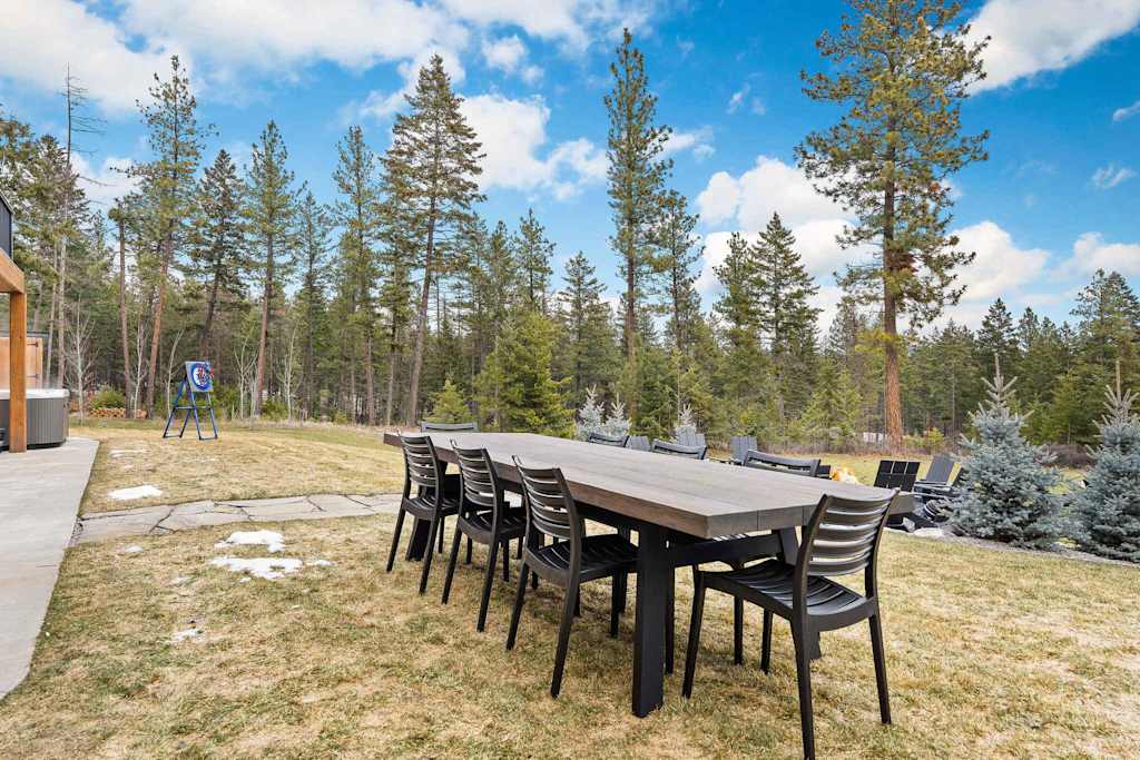 The Tamarack — long outdoor dining table and chairs set on a grassy lawn with forest background