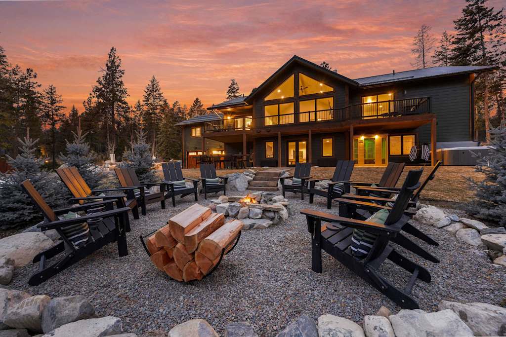 The Tamarack — gravel outdoor fire pit with chairs and firewood rack outside the illuminated lodge at dusk