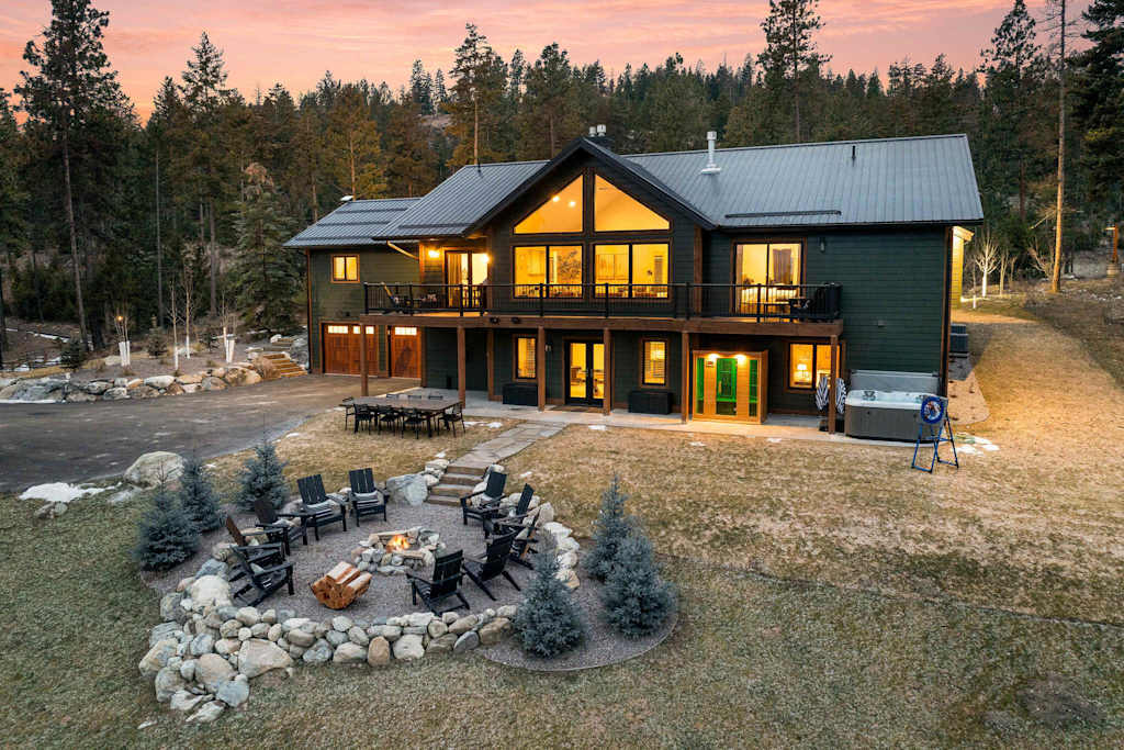 The Tamarack — rear view of multi-level lodge featuring fire pit seating, patio, and upper deck at dusk