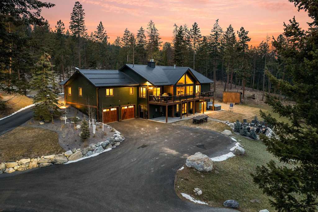 The Tamarack — elevated exterior view of lodge, paved driveway, garage, deck, and forest backdrop at sunset