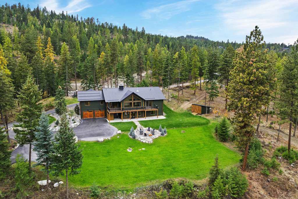 The Tamarack — aerial view of a dark green lodge nestled in a pine forest with a lawn and driveway