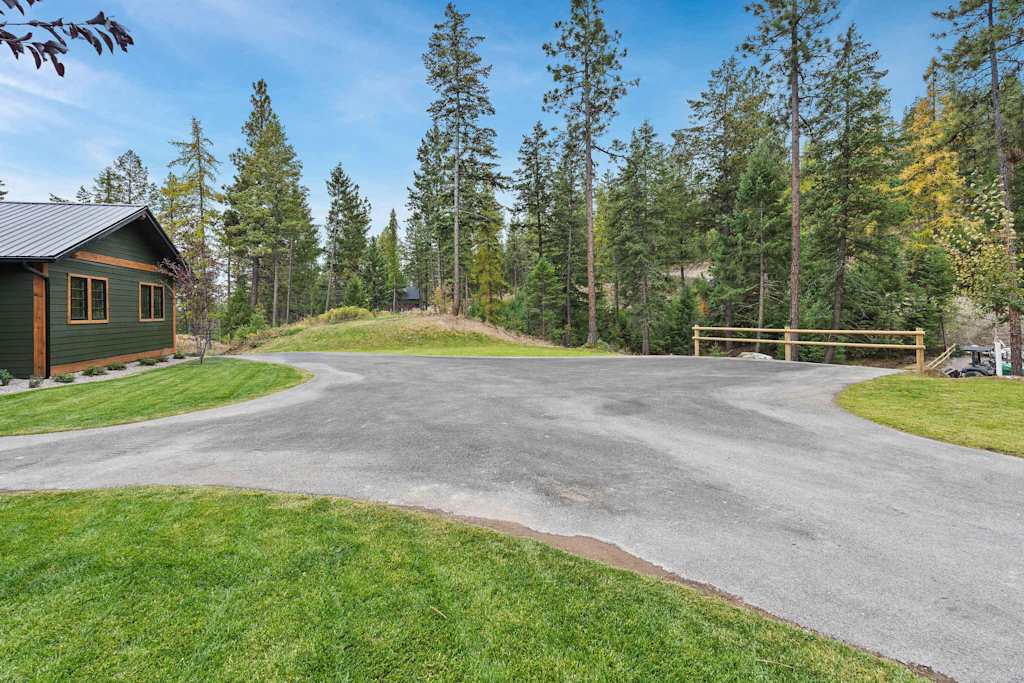 The Tamarack — paved driveway and turnaround area bordered by green lawn, a wooden fence, and pine trees