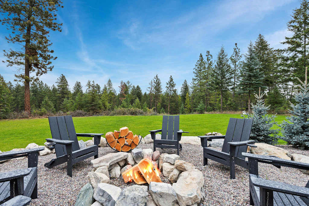 The Tamarack — stone fire pit with burning wood surrounded by adirondack chairs on a gravel patio