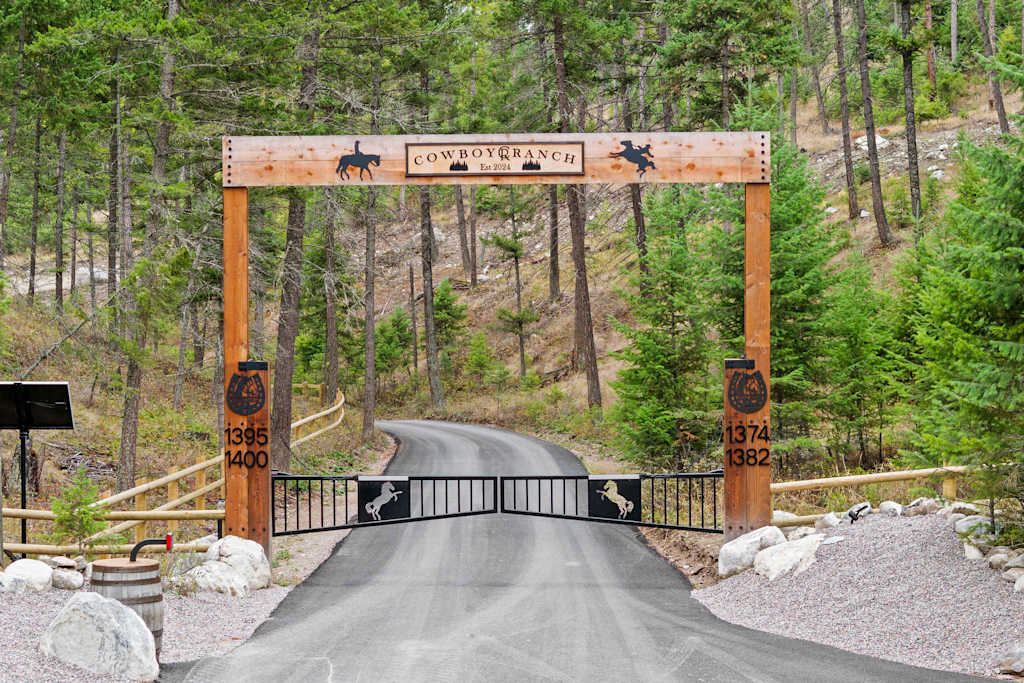The Tamarack — gated road entrance framed by a wooden archway sign reading cowboy ranch among pine trees