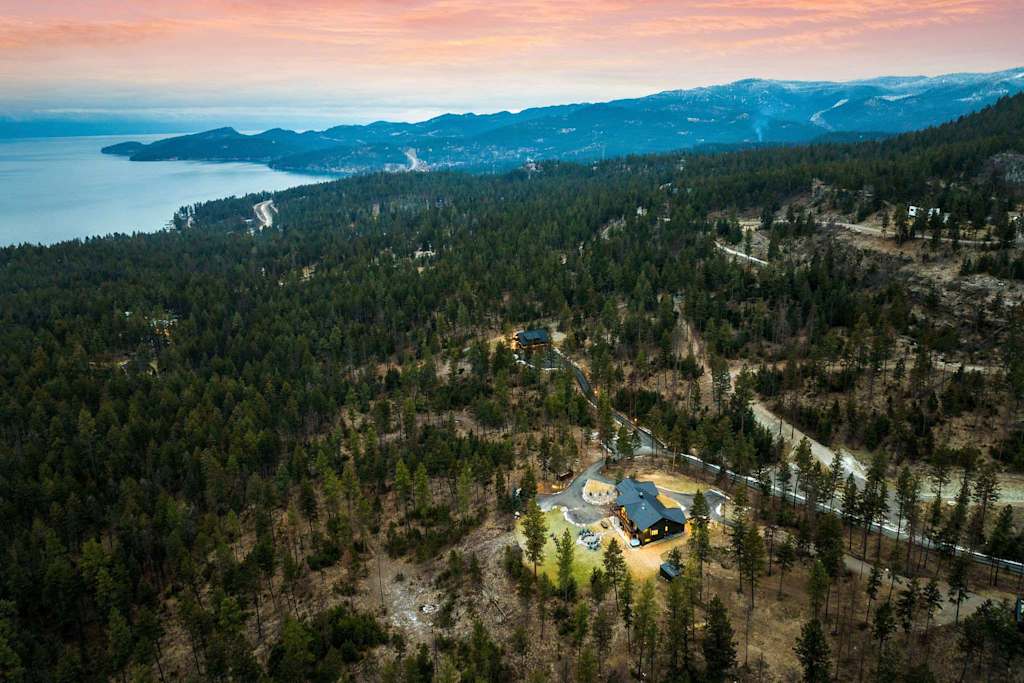 The Tamarack — aerial view of a lodge nestled in a pine forest overlooking a lake and mountains