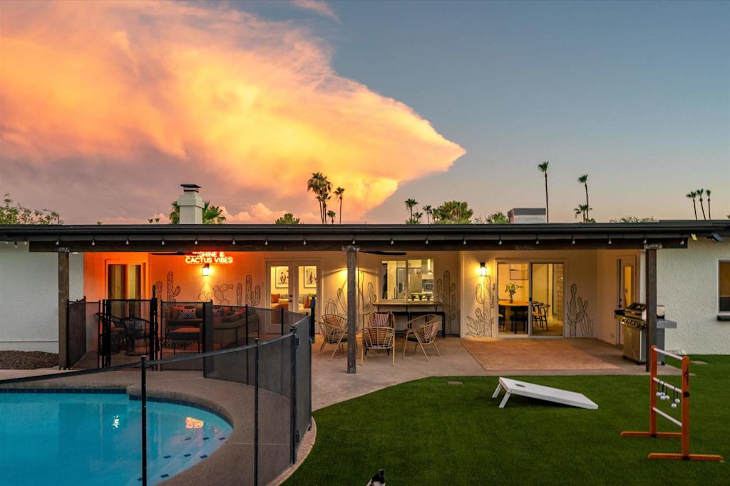 The Sunkiss — backyard patio with seating next to a fenced swimming pool and lawn games at sunset