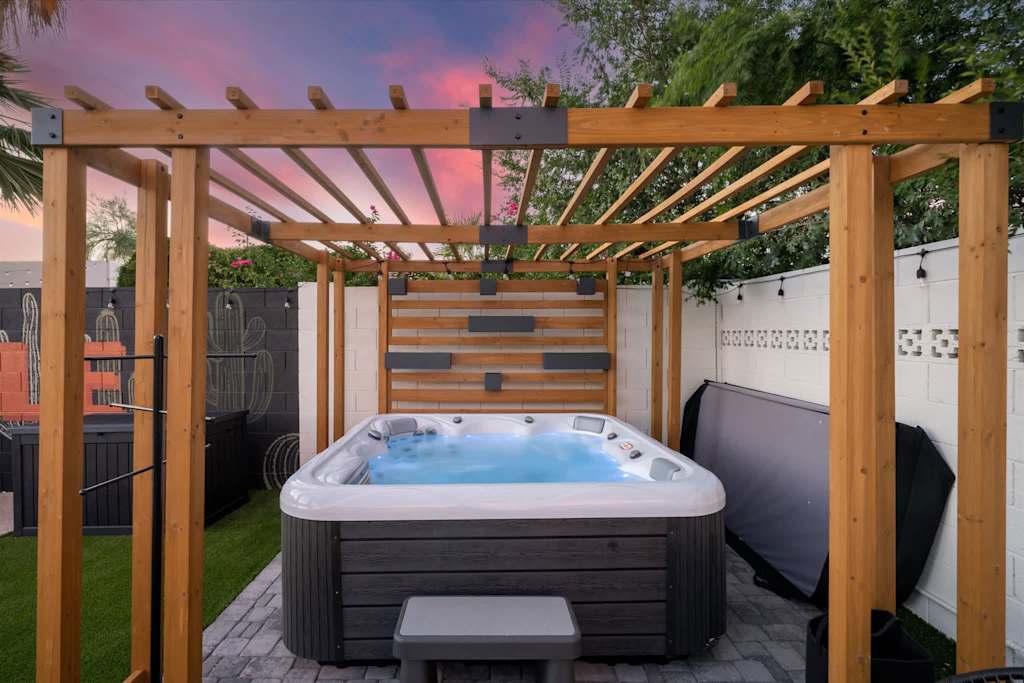 The Sunkiss — outdoor hot tub situated under a wooden pergola on a paver patio at sunset