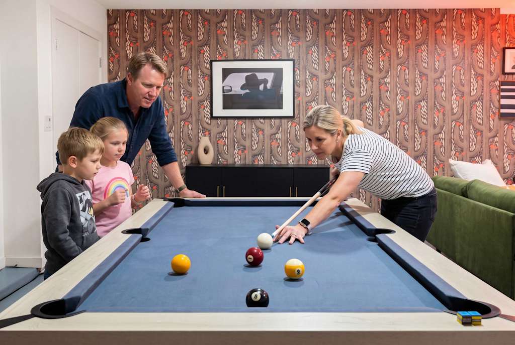 The Sunkiss — family gathered around a blue pool table playing billiards in a room with patterned wallpaper