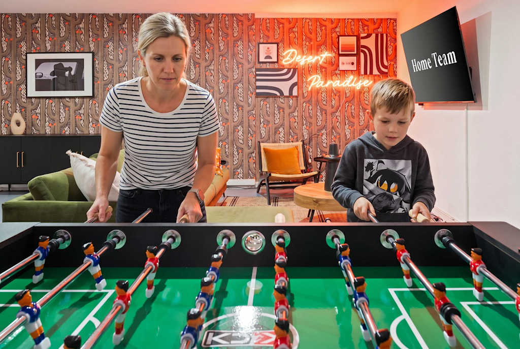 The Sunkiss — mother and son playing foosball in a game room with desert wallpaper and wall art