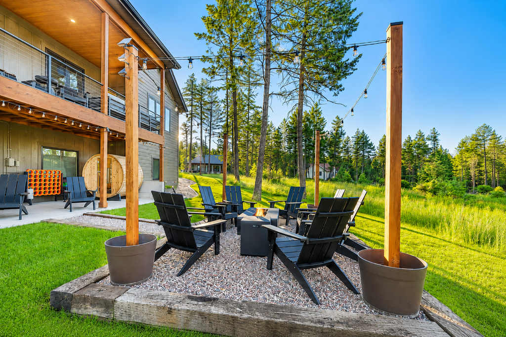The Evergreen — outdoor gravel patio featuring black adirondack chairs around a fire pit with string lights overhead