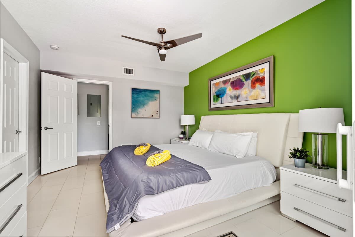 Pompano Condo: This bedroom has a bed, a ceiling fan and a bright green accent wall