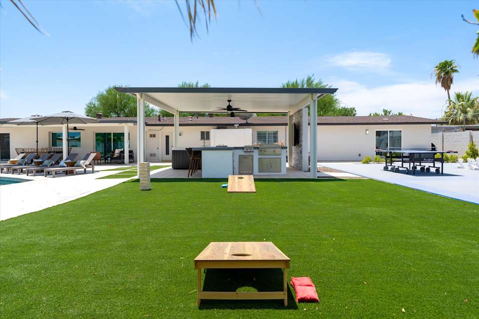 Synthetic turf lawn with cornhole and covered patio beyond