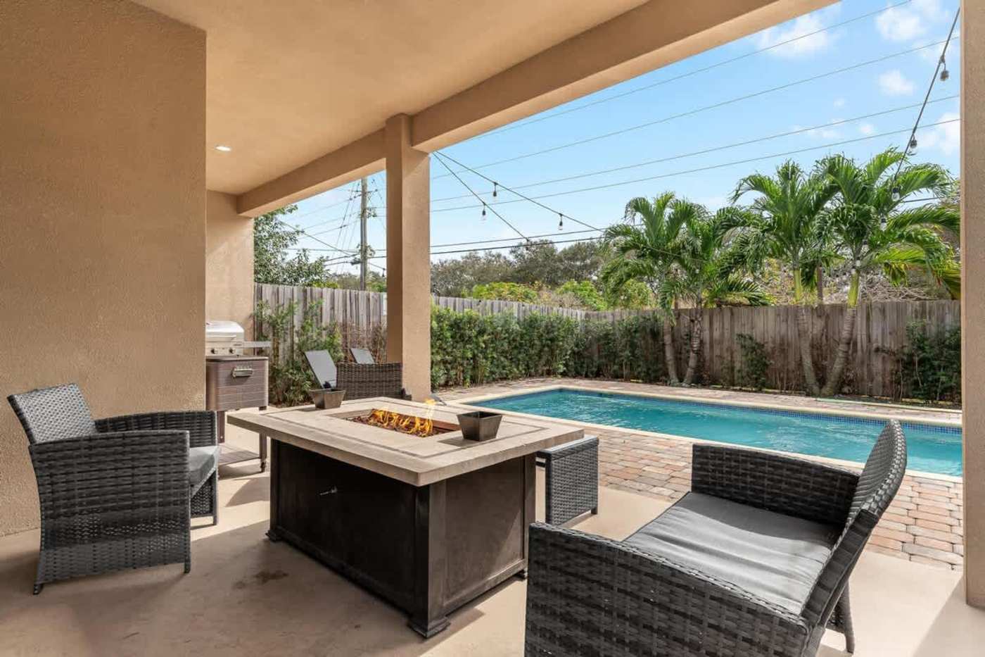 The Arcade House: Fire pit table and armchairs under the patio, beside the pool