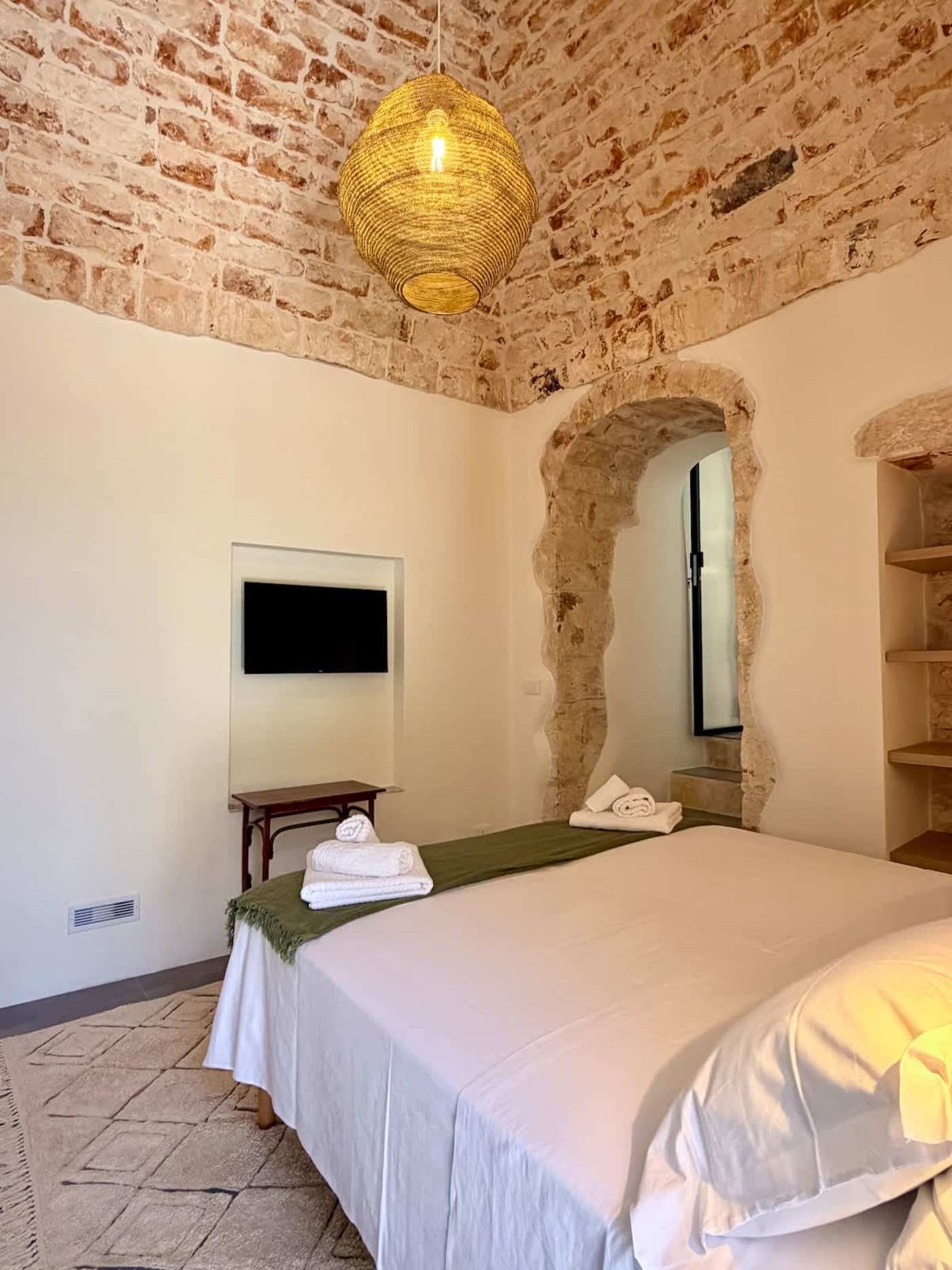 Trullo Ostro: Trullo bedroom with wall-mounted TV and arched stone doorway