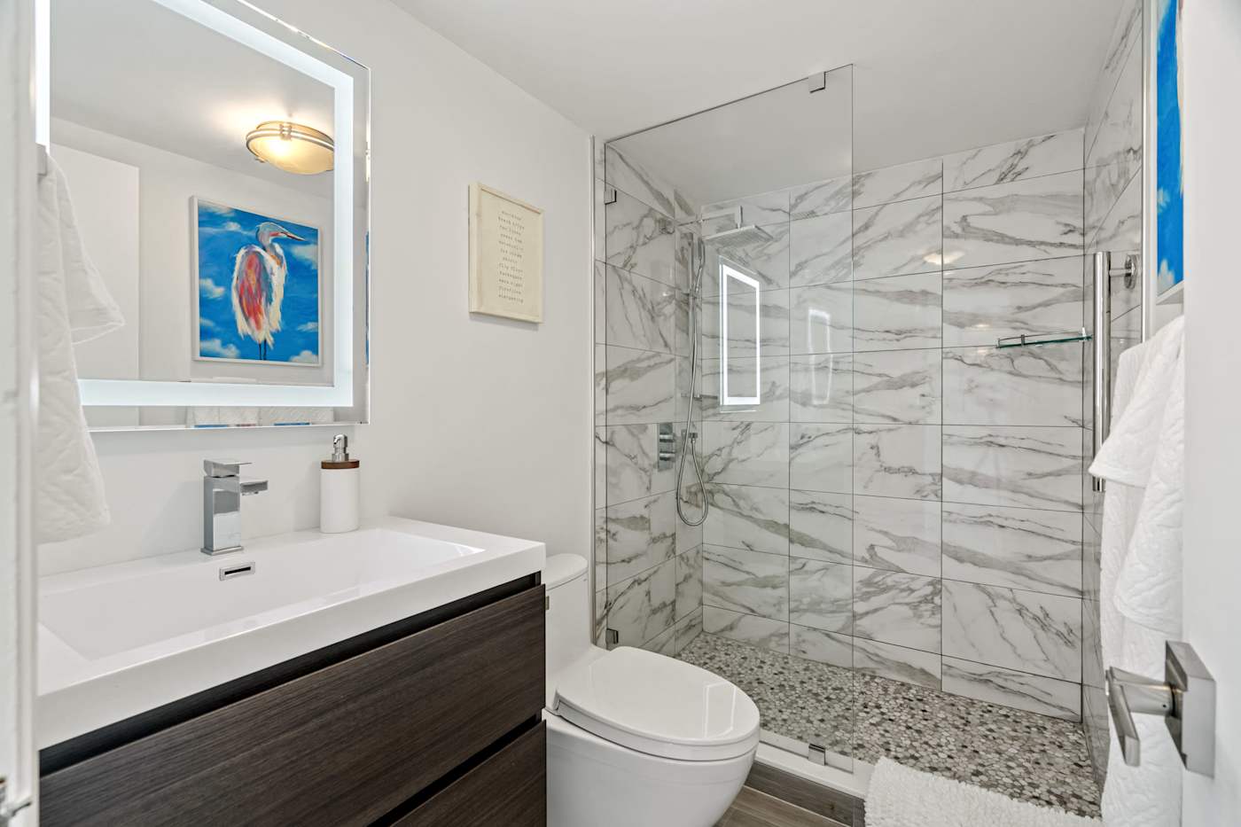Ocean Block: The bathroom has a lit mirror, a vanity and a glass walk-in shower
