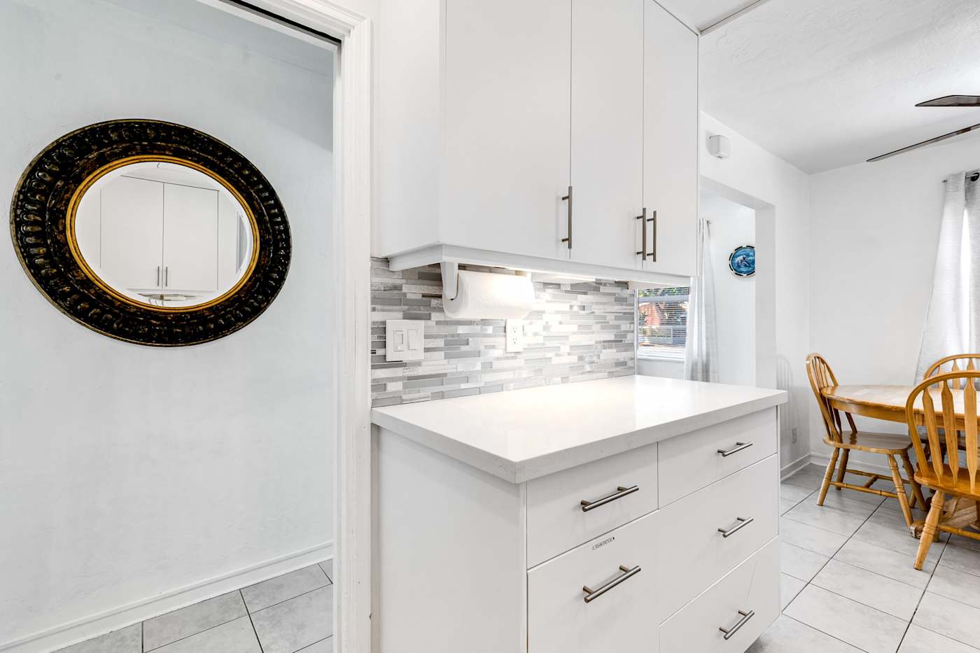 Pompano Bungalow: The kitchen has white cabinets and a tiled backsplash beside the dining nook