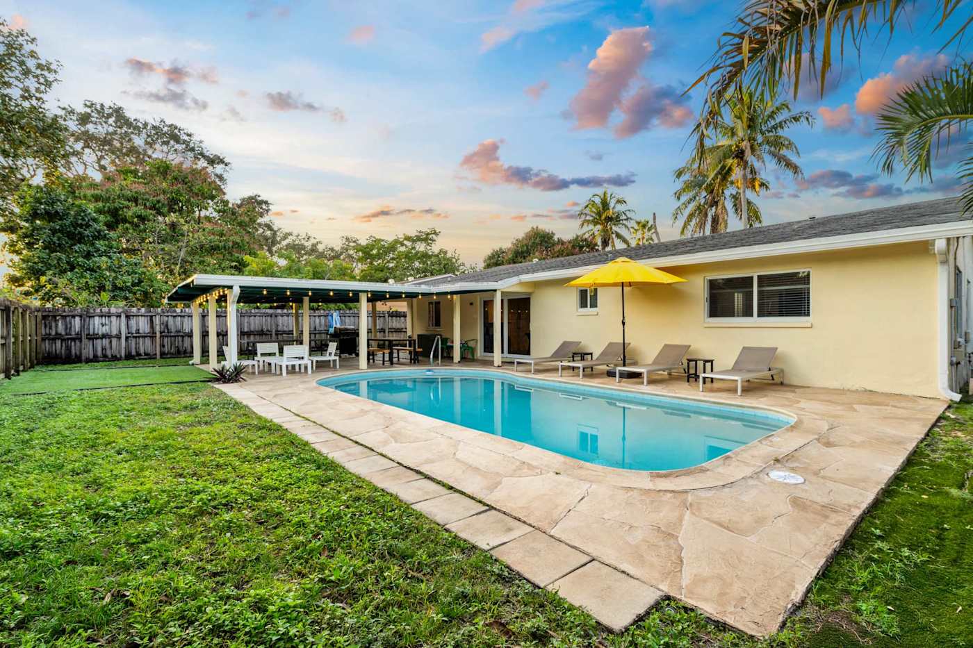 The Game House: Pool and lawn in daylight, with the covered patio behind