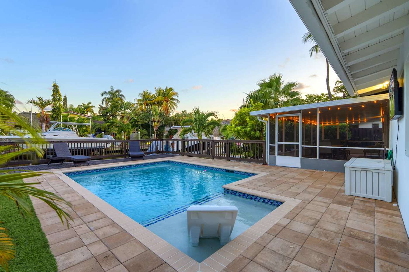 Canal House: Pool and paved deck at dusk, with the screened porch and canal