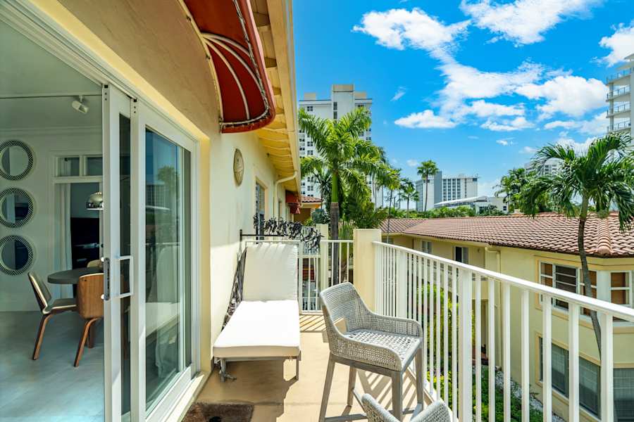 Ocean Block: The balcony has a lounge chair and seating, with palm trees beyond the railing