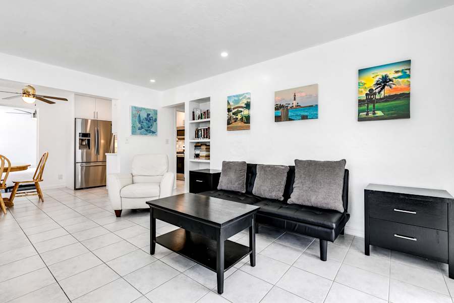 Pompano Bungalow: The living room has a black sofa, an armchair and colorful wall art