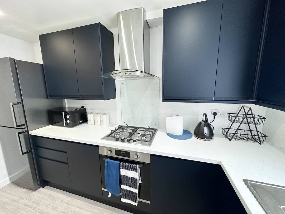 The kitchen at the Lewisham house: navy units, a white worktop, a gas hob and an extractor over it