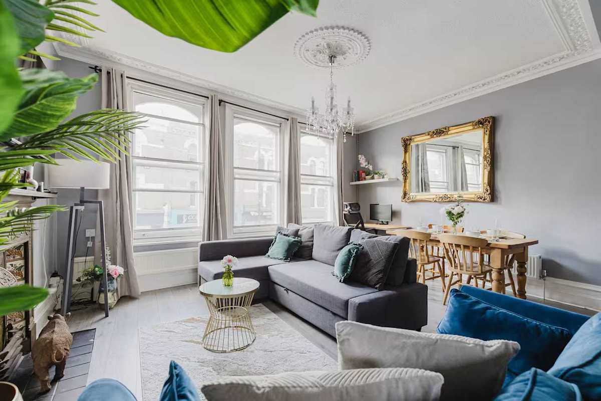 The living room at the Fulham maisonette: tall bay windows, a chandelier, grey sofas and a dining table at the far end