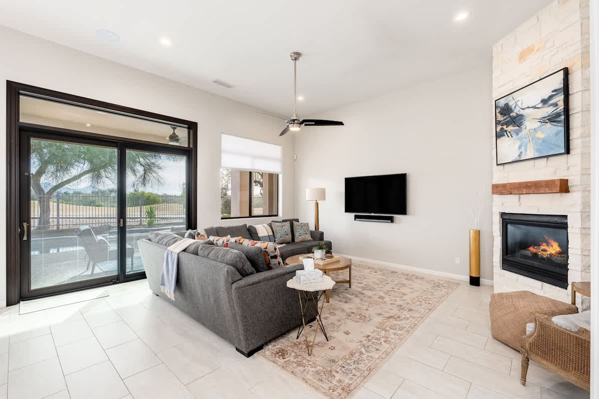 Sink into plush comfort in your spacious living room, where a cozy fireplace, modern entertainment setup, and serene outdoor views create your perfect retreat.