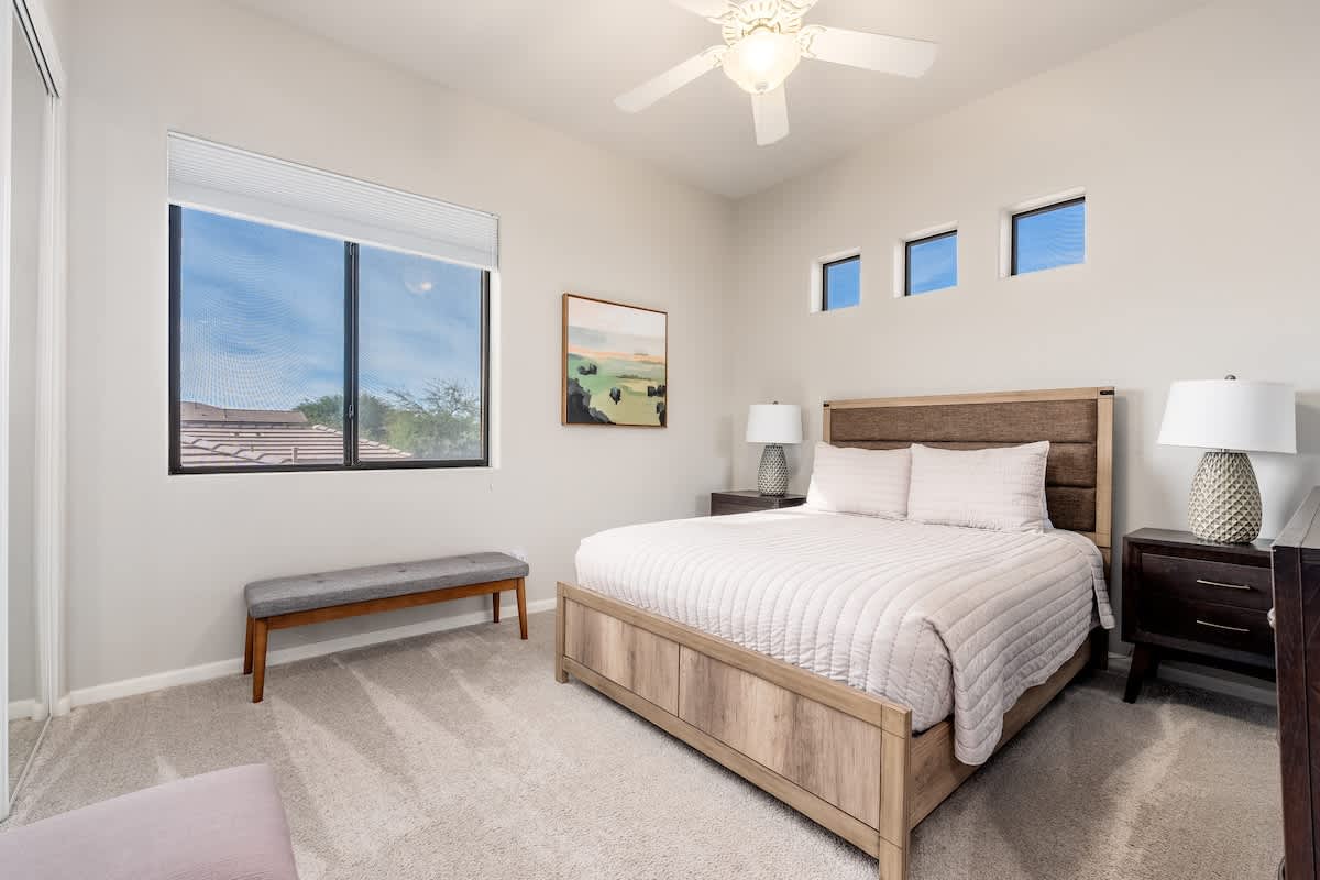 Unwind in your tranquil bedroom with a plush bed, gentle ceiling fan, and serene natural light streaming through large windows—your perfect sanctuary for restful sleep.