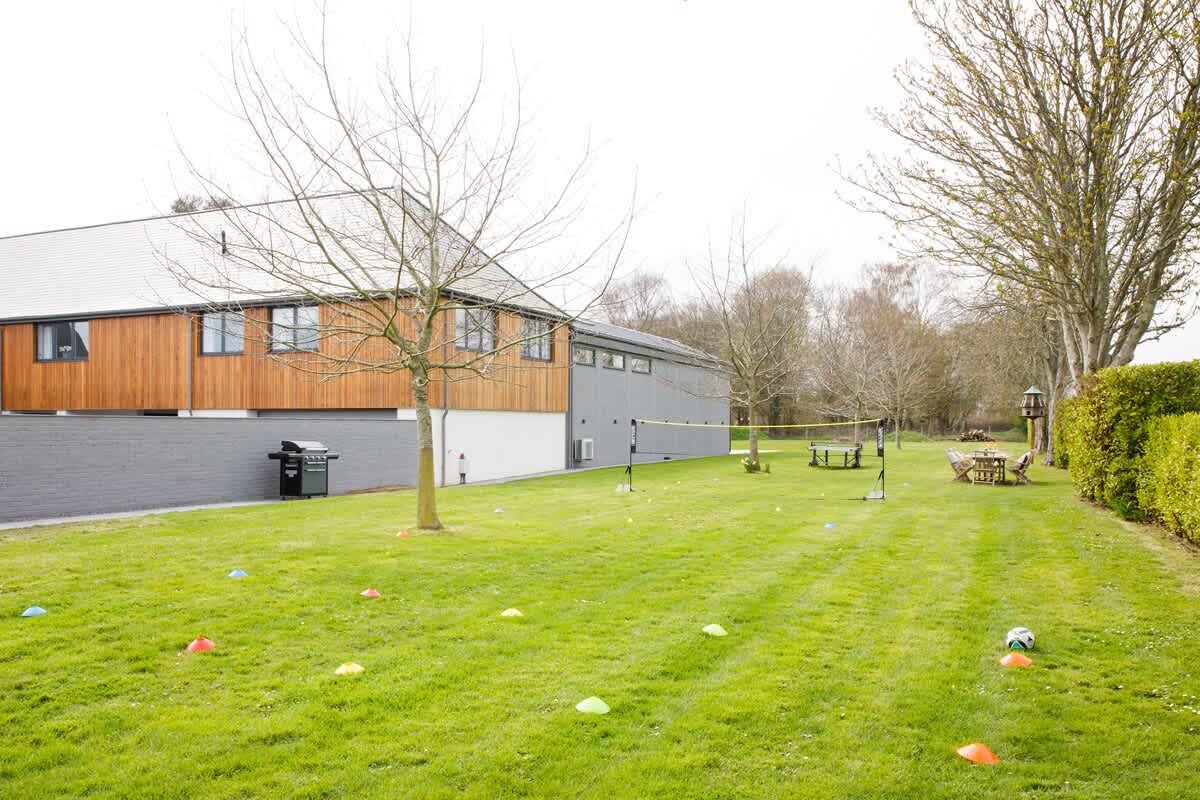 Spacious garden at Cedar House with a volleyball net, lawn games, and ample seating areas. A perfect setting for outdoor sports, picnics, or relaxing amidst greenery, ideal for families and group activities