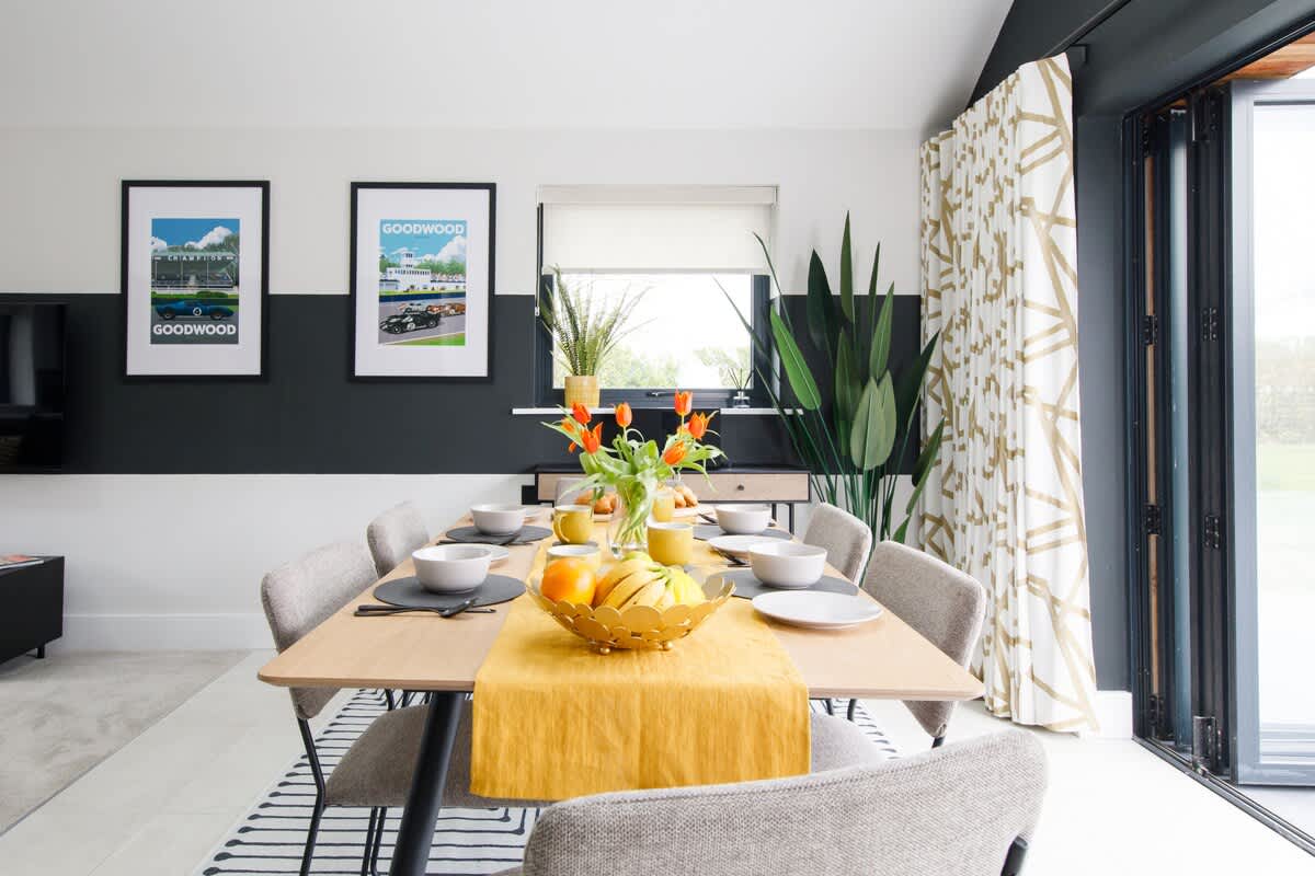 Cedar Lodge: Stylish dining area with a modern table set for eight, complemented by vibrant decor and bi-fold doors leading to the outdoors. Perfect for enjoying meals with natural light and scenic views, creating a welcoming and elegant atmosphere.