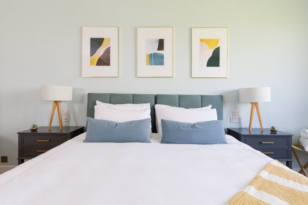 Bedroom 1 - Cedar House: Elegant bedroom featuring a plush king-size bed, modern abstract artwork, and stylish bedside tables with warm lighting. Crisp linens and vibrant decor create a serene and inviting space for a restful night’s sleep.