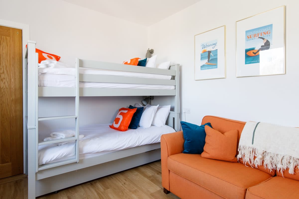 Bedroom 4 - Cedar House: Cozy bedroom with bunk beds, vibrant decor, and a comfortable orange sofa. Features playful surf-themed artwork and fresh linens, perfect for kids or extra guests to enjoy a fun and relaxing stay