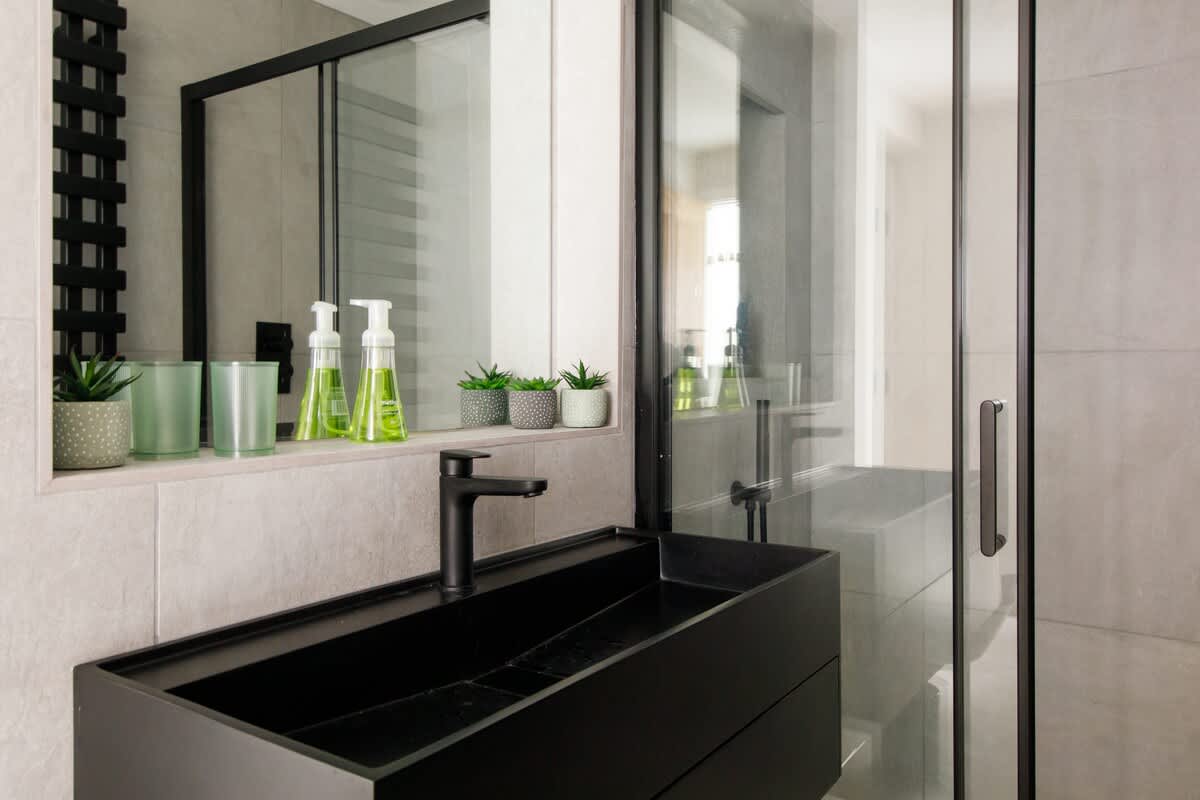 Cedar Lodge: Stylish modern bathroom featuring a sleek black sink, glass-enclosed shower, and elegant decor. Includes thoughtful amenities and lush green accents, creating a functional yet luxurious space for your comfort.