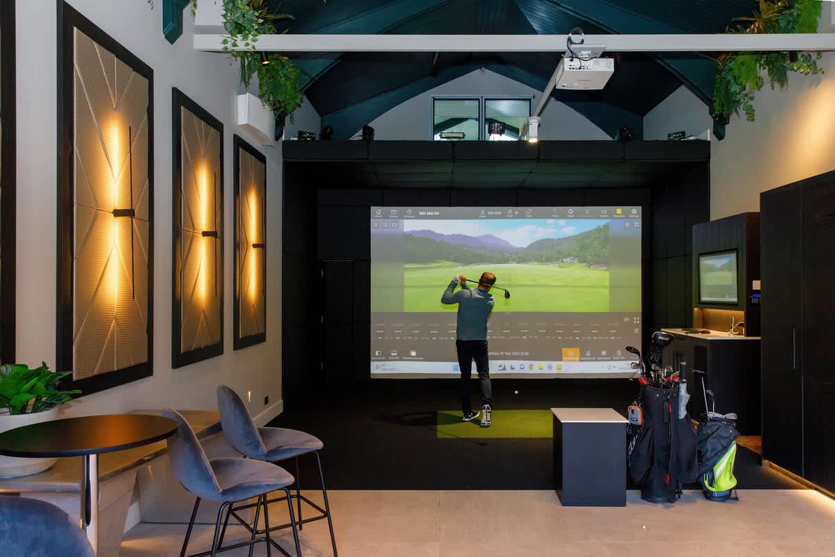 Indoor golf simulator in a stylish, modern space with seating and ambient lighting. Perfect for honing your swing or enjoying a fun activity regardless of weather. Additional charges may apply for use of the simulator. Ideal for golf enthusiasts!