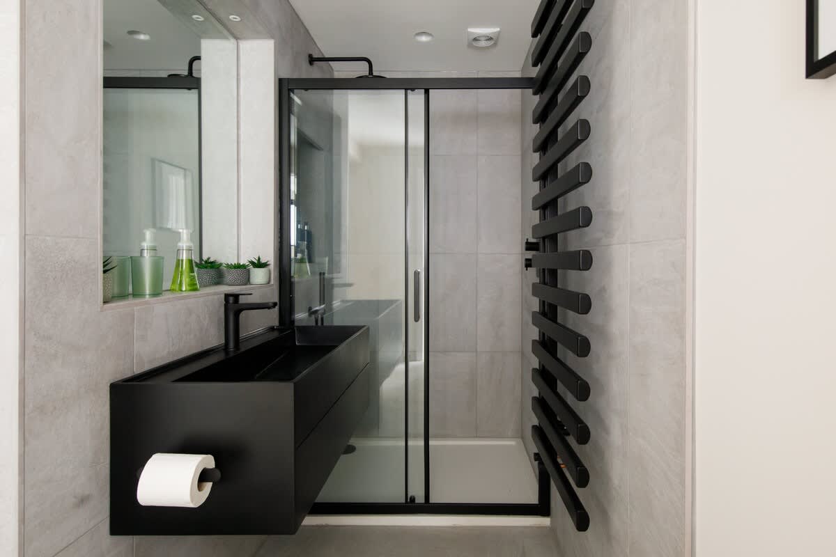 Cedar Lodge: Contemporary bathroom with a sleek black vanity, glass walk-in shower, and modern heated towel rail. Thoughtfully designed with elegant finishes and practical amenities for a luxurious and comfortable experience.