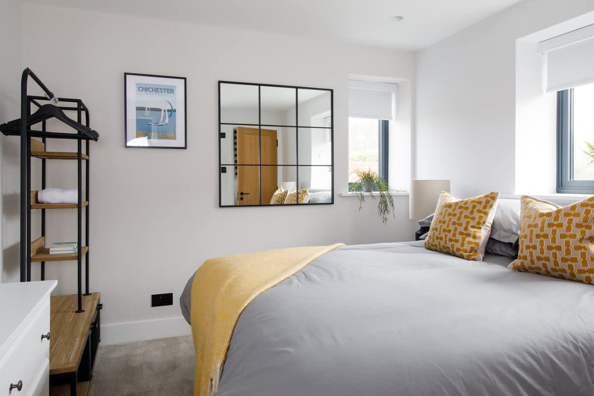 Cedar Lodge: Bright and modern bedroom featuring a cozy double bed with vibrant accents, stylish mirror, and open wardrobe. Natural light fills the space, creating a warm and inviting atmosphere perfect for relaxation and comfort.