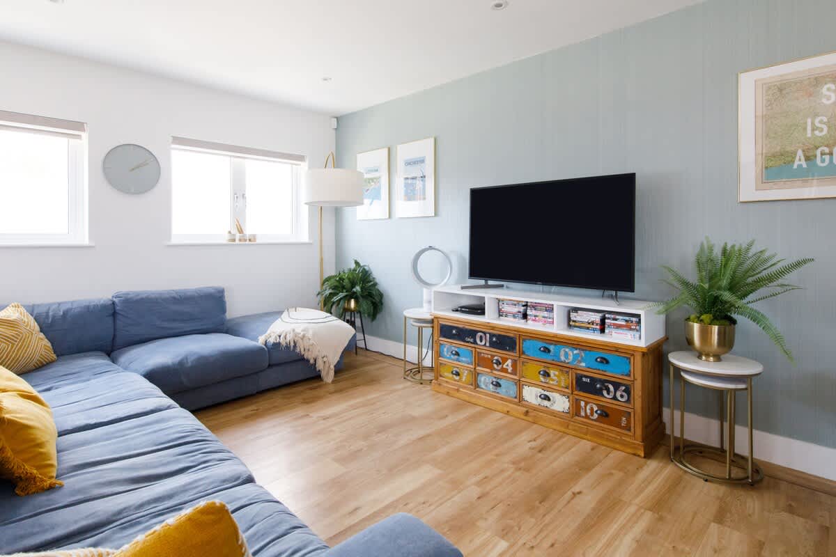 Cedar House: Relax in this cozy living room with a large plush sectional sofa, vibrant decor, and a flat-screen TV. Features unique furniture, stylish accents, and plenty of natural light, creating a perfect space for unwinding or entertaining.