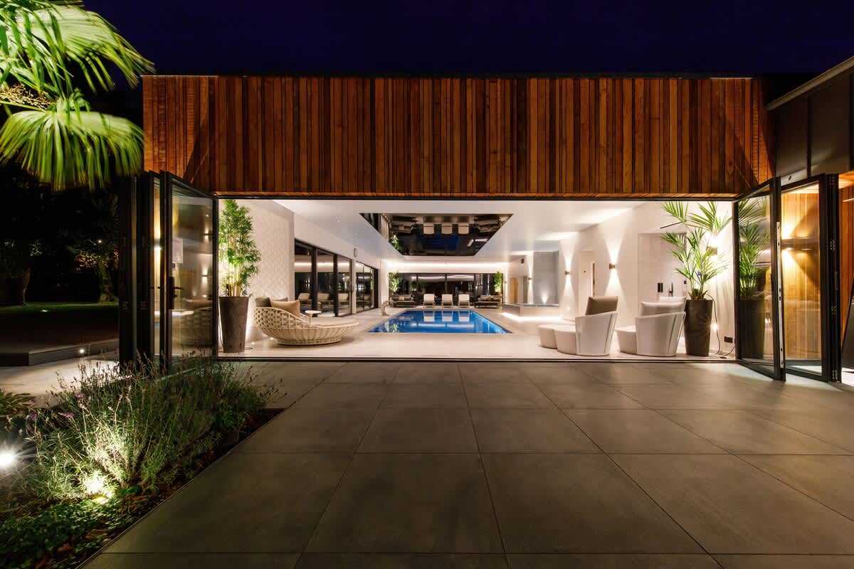 Luxurious indoor pool area with floor-to-ceiling windows, elegant seating, and ambient lighting. Perfect for a relaxing evening swim or unwinding in style. Experience ultimate comfort in this stunning, modern retreat ((extra charges apply))